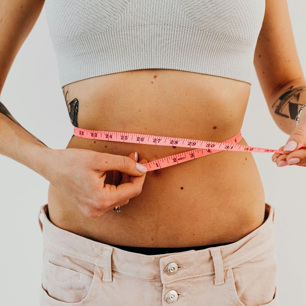 MICC injection concept with person measuring waist using pink measuring tape to represent fat metabolism and energy boost.